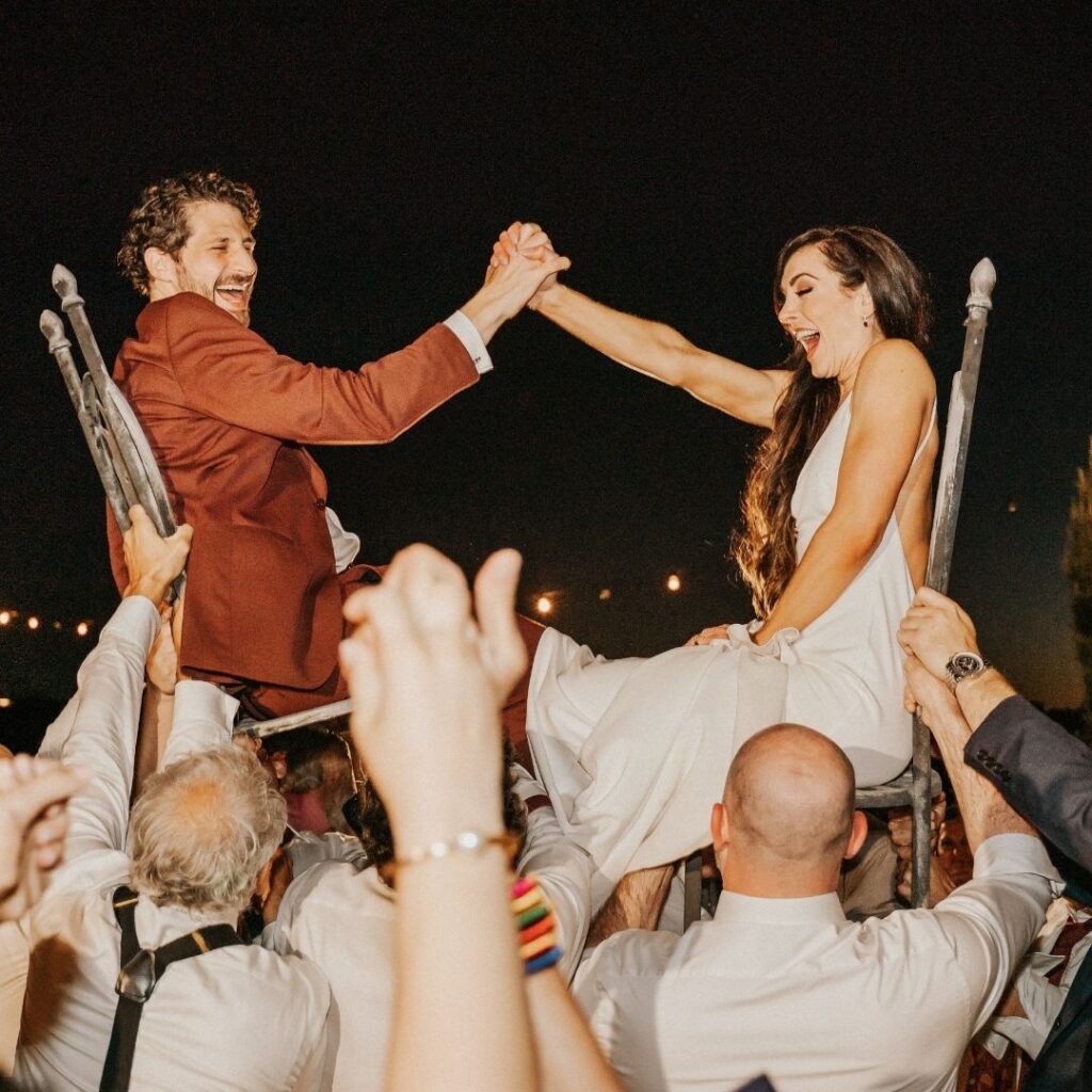 guests carrying bride and groom in chairs at their luxury wedding
